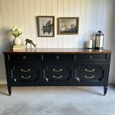 a black dresser with gold handles and drawers in front of two pictures on the wall