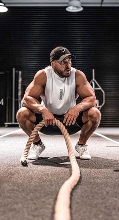 a man squatting down while holding a rope