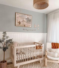 a baby's room with a crib, rocking chair and potted plant