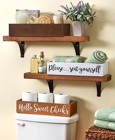 two shelves above a toilet with towels and soaps on them, next to a towel rack that says please say yourself