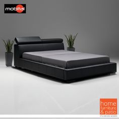 a black leather bed with plant in the corner and grey wall behind it, on a white floor