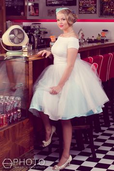 a woman in a white dress is standing by a counter with sodas on it