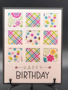 a happy birthday card with colorful squares and flowers on it's front, sitting on a black stand