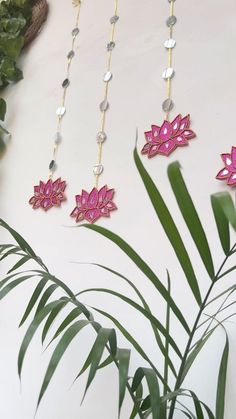 three pink and gold necklaces hanging on a white wall next to a green plant