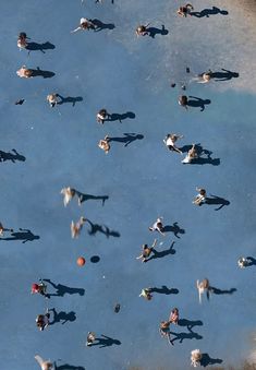 many people are swimming and playing in the blue water with their shadows on the ground