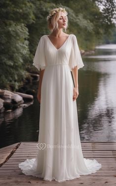 a woman in a white dress standing on a dock by the water wearing a flower crown