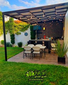 an outdoor kitchen and dining area in a backyard with lights strung from the roof over it