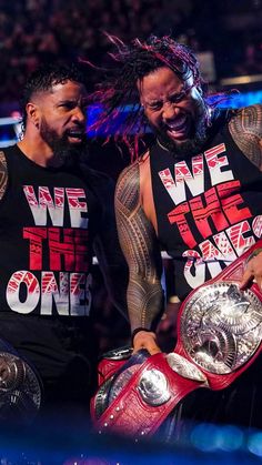 two men standing next to each other with their arms around one another holding the same wrestling belts
