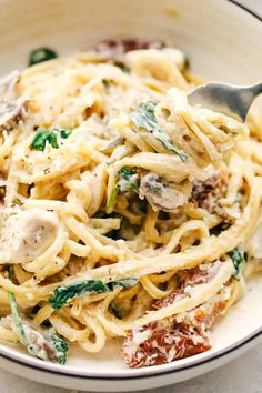 a white bowl filled with pasta, mushrooms and spinach on top of a table