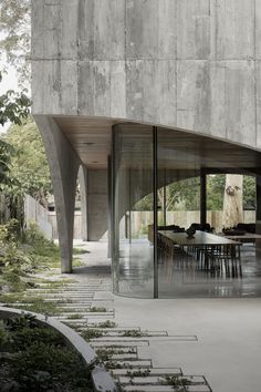 an outdoor dining area with tables and chairs in front of a concrete building that has glass walls