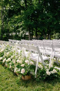 rows of white chairs are lined up in the grass for an outdoor wedding ceremony with flowers and greenery