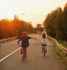 two people riding bikes on a road with trees in the background and one person raising their arms