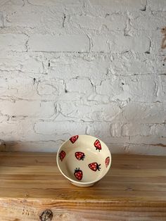 a bowl with strawberries painted on it sitting on a wooden table next to a brick wall