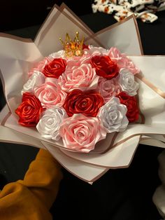 a bouquet of roses with a crown on top is being held by someone's hand