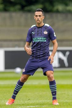 a man standing on top of a soccer field wearing a purple shirt and blue shorts