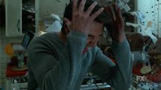 a man holding his hands up to his head in front of a messy kitchen area