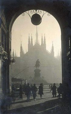 an old black and white photo of people walking in front of a building with spires