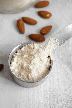 almonds and powdered sugar in a measuring spoon on a white tablecloth next to a jar