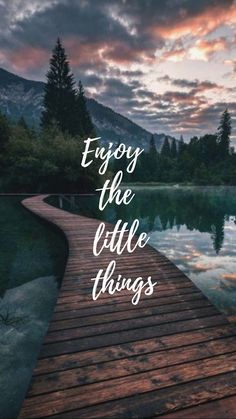 a wooden dock with the words enjoy the little things written on it in front of a lake