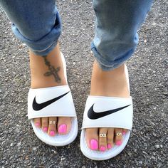 a woman's feet with pink and white nail polishes on them, while wearing nike slides