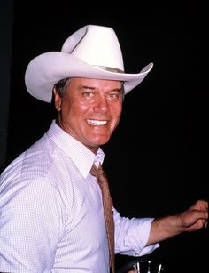 a man wearing a white cowboy hat and tie with his hand out to the side