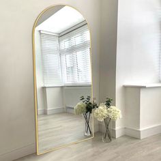 a mirror sitting on top of a wooden floor next to a vase filled with flowers