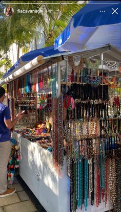 a woman standing in front of a market stall selling necklaces and bracelets on display