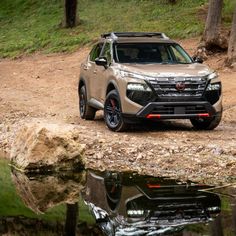 the front end of a silver suv parked on a dirt road near water and trees