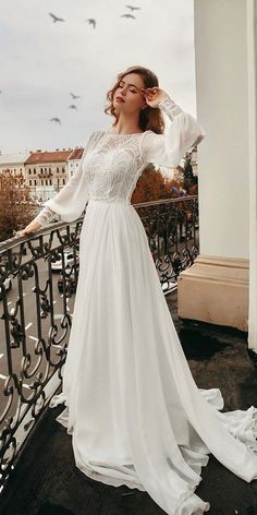 a woman is standing on a balcony wearing a white wedding dress with long sleeves and an open back