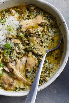 a white bowl filled with chicken, rice and spinach soup next to a spoon