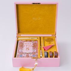 an open pink box filled with assorted items on top of a white table next to a tassel