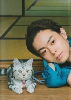 a man laying on the floor next to a gray and white cat with green eyes