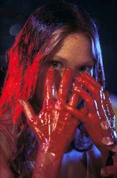 a woman covered in red liquid holding her hands up to her face and looking at the camera