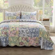 a bed with a flowered bedspread and matching comforter in front of a window