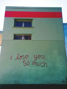 graffiti on the side of a building that says i love you so much and someone is looking out the window