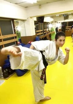 a woman doing karate in a gym with other people behind her and on the ground