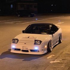 a white sports car parked in a parking lot with its lights turned on at night