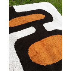 a black, orange and white rug with the letter s on it in grass area