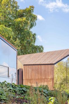 the house is made out of wood and has large windows on one side, along with plants