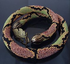 two bracelets with beads and metal clasps on a black surface, one has a leaf brooch