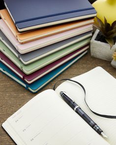 an open notebook with a pen sitting on top of it next to a flower pot