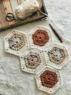 four crocheted hexagons sitting on top of a white rug next to yarn and scissors