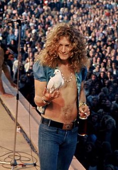 a man with long hair holding a white dog in front of a large group of people