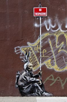 a painting of a person sitting on the ground next to a wall with graffiti written on it
