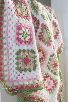 a crocheted blanket hanging from the side of a door with pink, green and white flowers on it