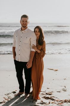 an engaged couple standing on the beach in front of the ocean during their engagement session