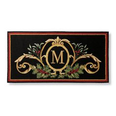 a christmas door mat with the letter m in gold and green leaves on black background