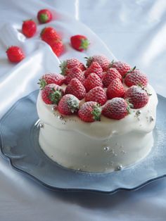 a cake with white frosting and fresh strawberries on top is sitting on a blue plate