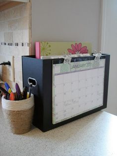 a desk with a calendar, pen holder and other office supplies on it's side