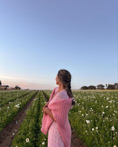 a woman in a pink dress standing in a field with white flowers and looking up at the sky